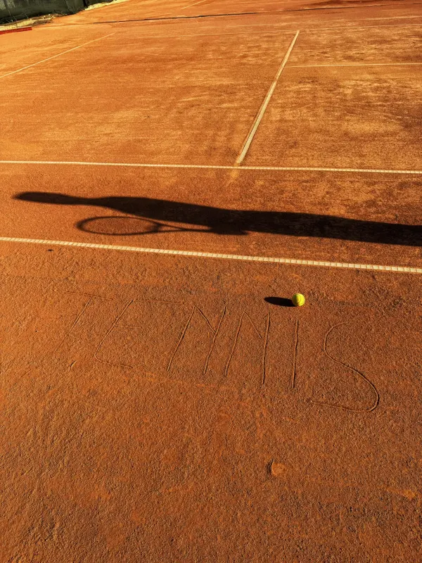 Zgură la apus, cu umbra unui jucător și cuvântul TENIS scris în zgură